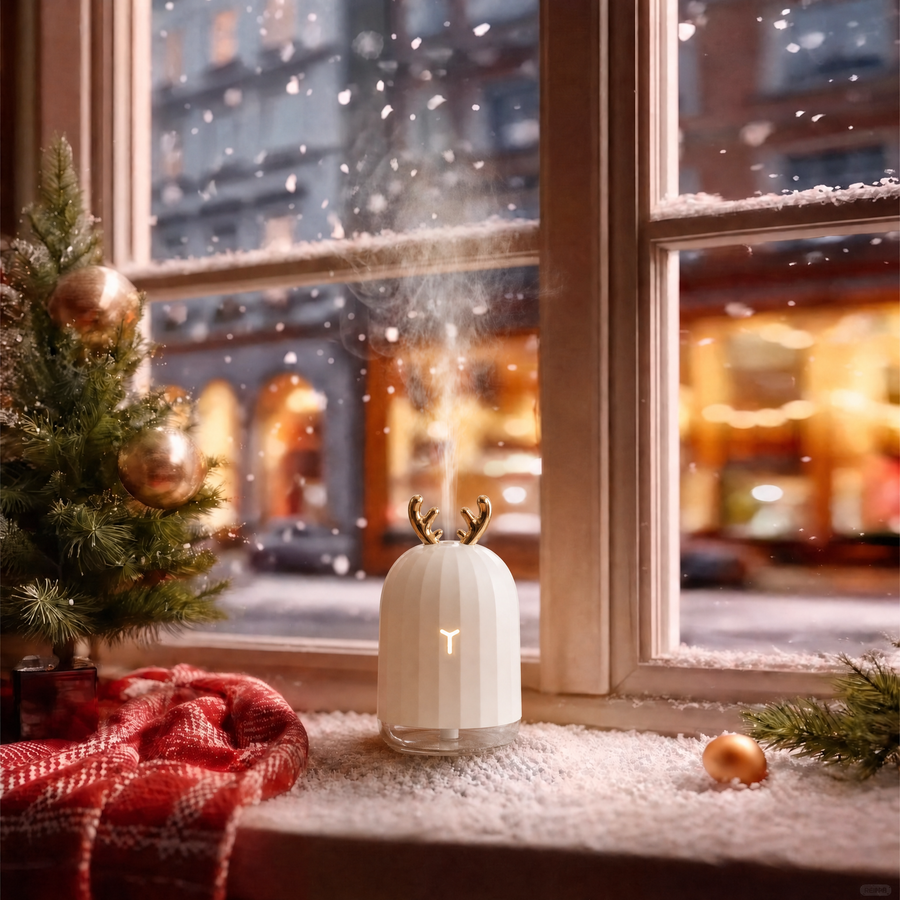 Cute deer white humidifier with essential oil set featuring golden antlers and mist on a snowy Christmas windowsill, decorated with a small Christmas tree, red plaid blanket, and gold ornaments, creating a cozy winter holiday ambience and ideal Christmas gift.