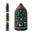 Front view of the dark wood grain star cutout diffuser emitting blue LED light with control buttons visible, alongside 3 bottles of essential oils (Lavender, Tea Tree, Sweet Orange).