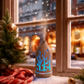 Glowing forest cutouts light wood ultrasonic aromatherapy diffuser with blue LED light and mist on a snowy Christmas windowsill, decorated with a small Christmas tree, red plaid blanket, and gold ornaments, creating a cozy winter holiday ambience and ideal Christmas gift.
