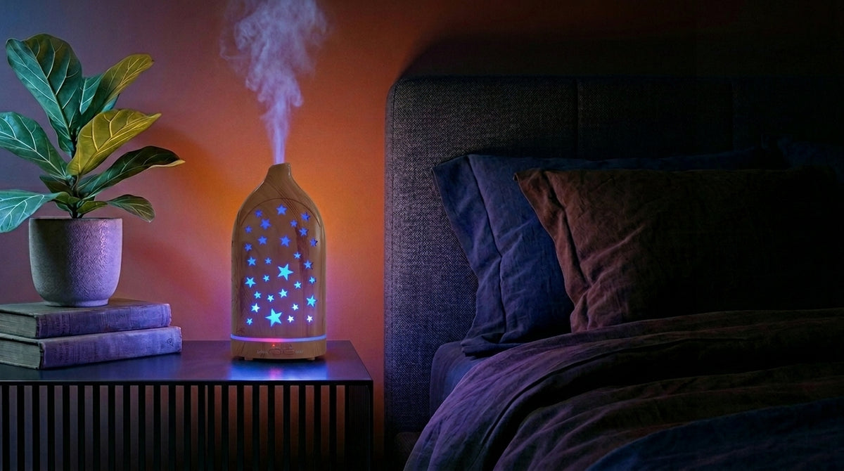 Light wood star cutout diffuser emitting a blue glow on a modern nightstand in a dark bedroom, next to a fiddle leaf fig plant and a cozy bed.