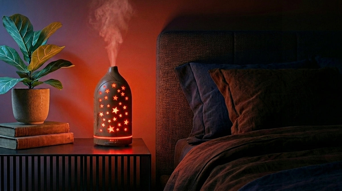 Light wood star cutout diffuser emitting a red glow on a modern nightstand in a dark bedroom, next to a fiddle leaf fig plant and a cozy bed.