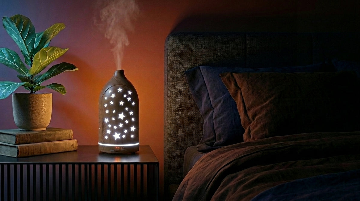 Light wood star cutout diffuser emitting a sky blue glow on a modern nightstand in a dark bedroom, next to a fiddle leaf fig plant and a cozy bed.