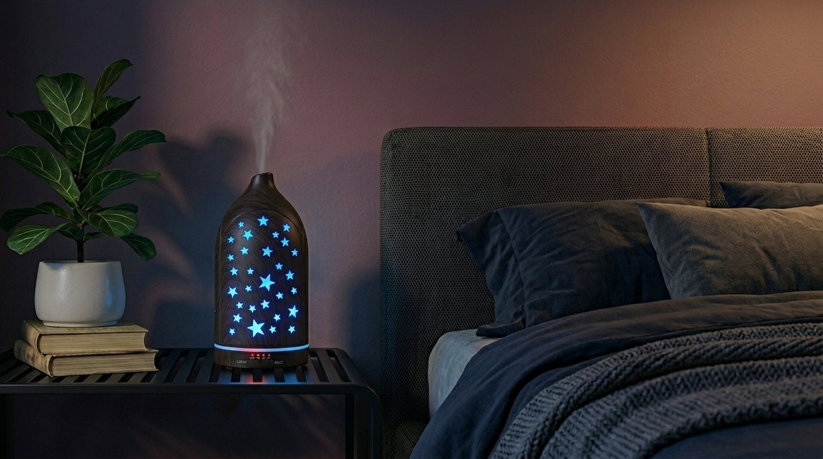 Dark wood grain star cutout diffuser emitting a calming blue starlight glow on a modern nightstand in a dimly lit bedroom, next to a fiddle leaf fig plant.