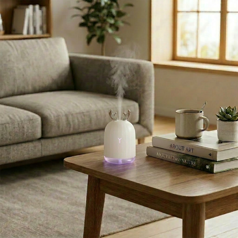 White deer design humidifier on a wooden coffee table in a bright living room, creating a relaxing atmosphere with a cup of coffee and art books.
