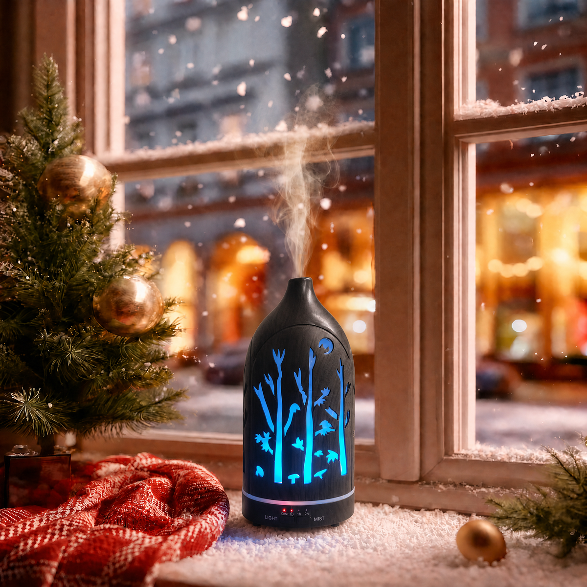 Glowing forest cutouts dark wood ultrasonic aromatherapy diffuser with blue LED light and mist on a snowy Christmas windowsill, decorated with a small Christmas tree, red plaid blanket, and gold ornaments, creating a cozy winter holiday ambience and ideal Christmas gift.