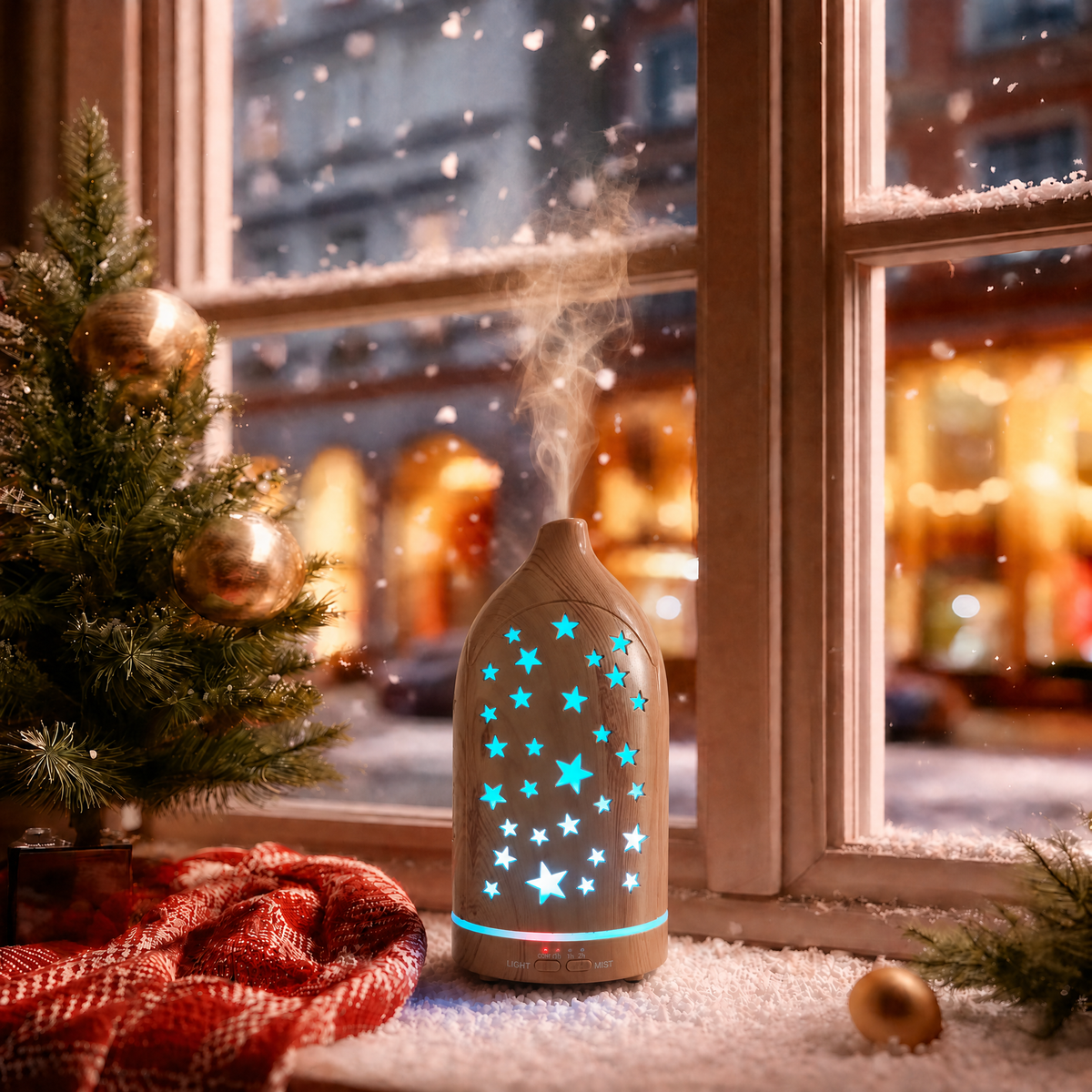 Glowing star cutouts light wood ultrasonic aromatherapy diffuser with blue LED stars and mist on a snowy Christmas windowsill, decorated with a small Christmas tree, red plaid blanket, and gold ornaments, creating a cozy winter holiday ambience and ideal Christmas gift.