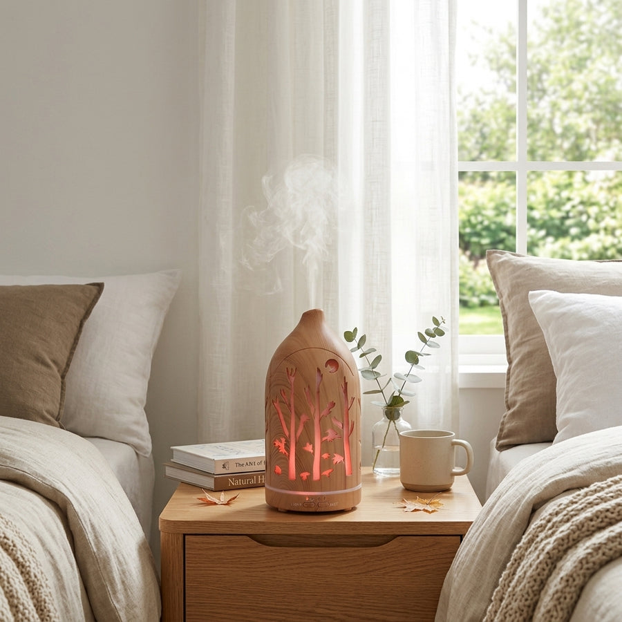 Light wood grain forest diffuser glowing with warm red/orange light on a nightstand between two beds, creating a relaxing bedroom atmosphere with eucalyptus leaves.
