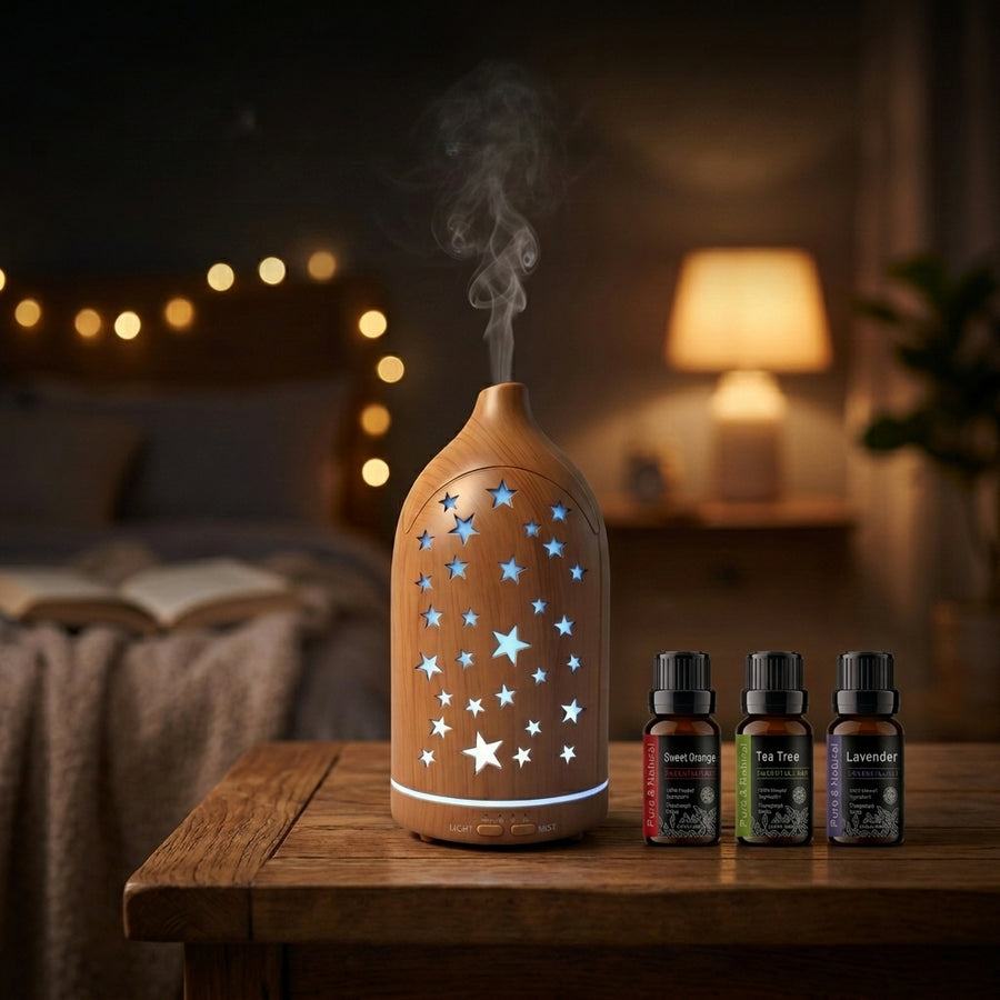 Light wood grain star cutout diffuser emitting blue LED light on a wooden nightstand in a cozy bedroom with fairy lights, accompanied by Sweet Orange, Tea Tree, and Lavender essential oils.