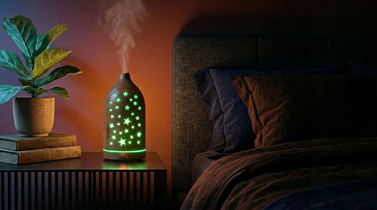 Light wood star cutout diffuser emitting a green glow on a modern nightstand in a dark bedroom, next to a fiddle leaf fig plant and a cozy bed.