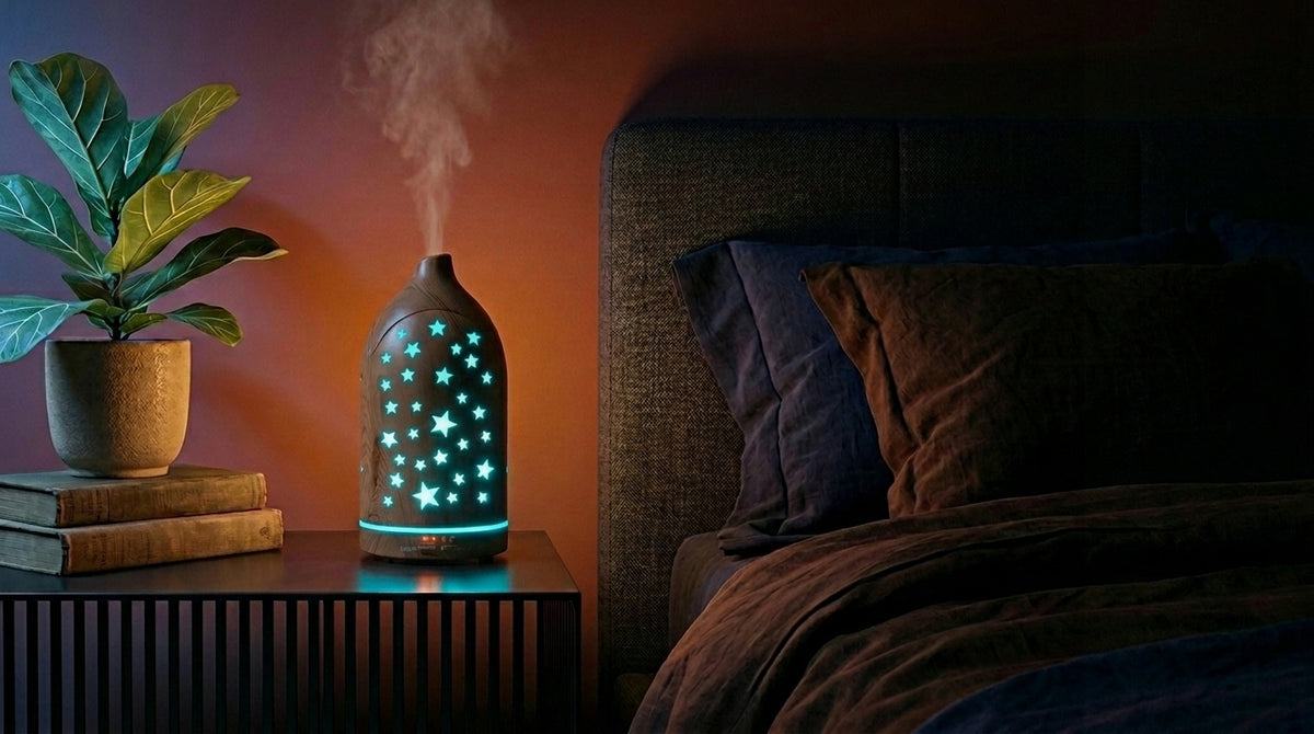 Light wood star cutout diffuser emitting a light blue glow on a modern nightstand in a dark bedroom, next to a fiddle leaf fig plant and a cozy bed.