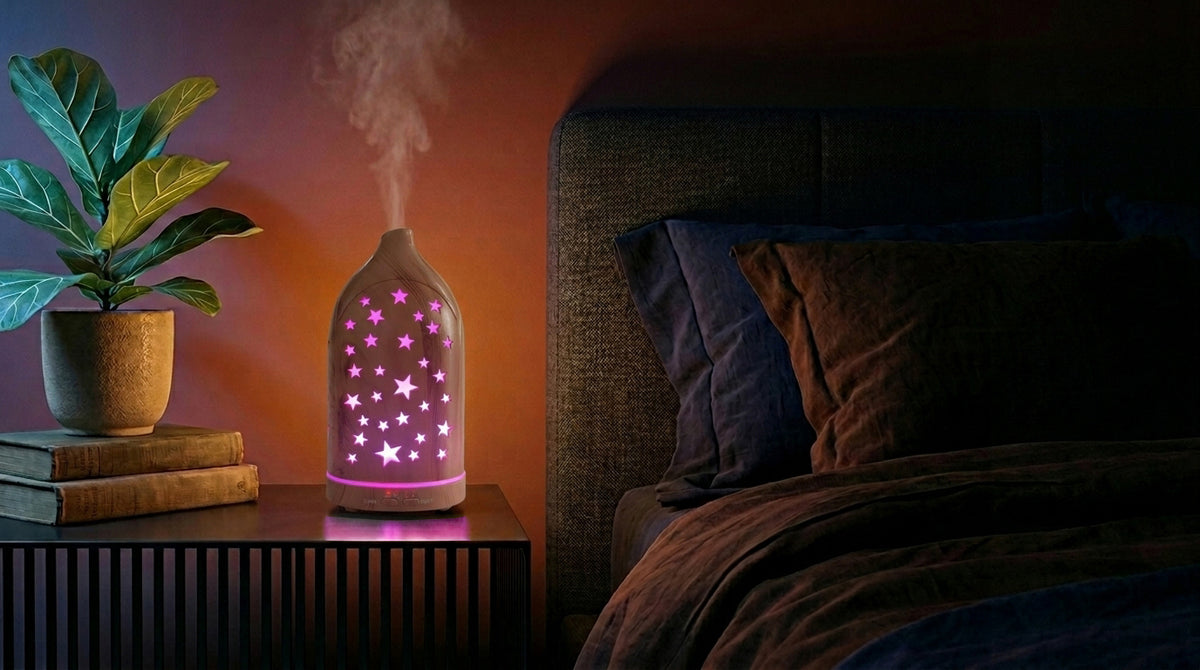 Light wood star cutout diffuser emitting a purple glow on a modern nightstand in a dark bedroom, next to a fiddle leaf fig plant and a cozy bed.