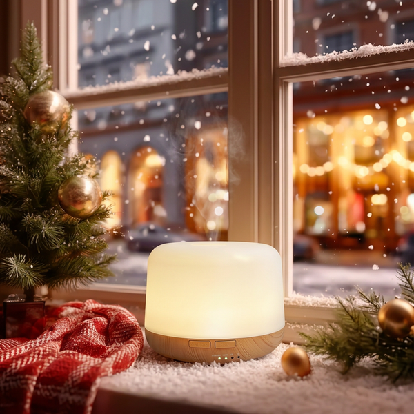 Mini light wood diffuser glowing with warm light and mist on a snowy Christmas windowsill, decorated with a small Christmas tree, red plaid blanket, and gold ornaments, perfect for cozy winter holiday home ambience.